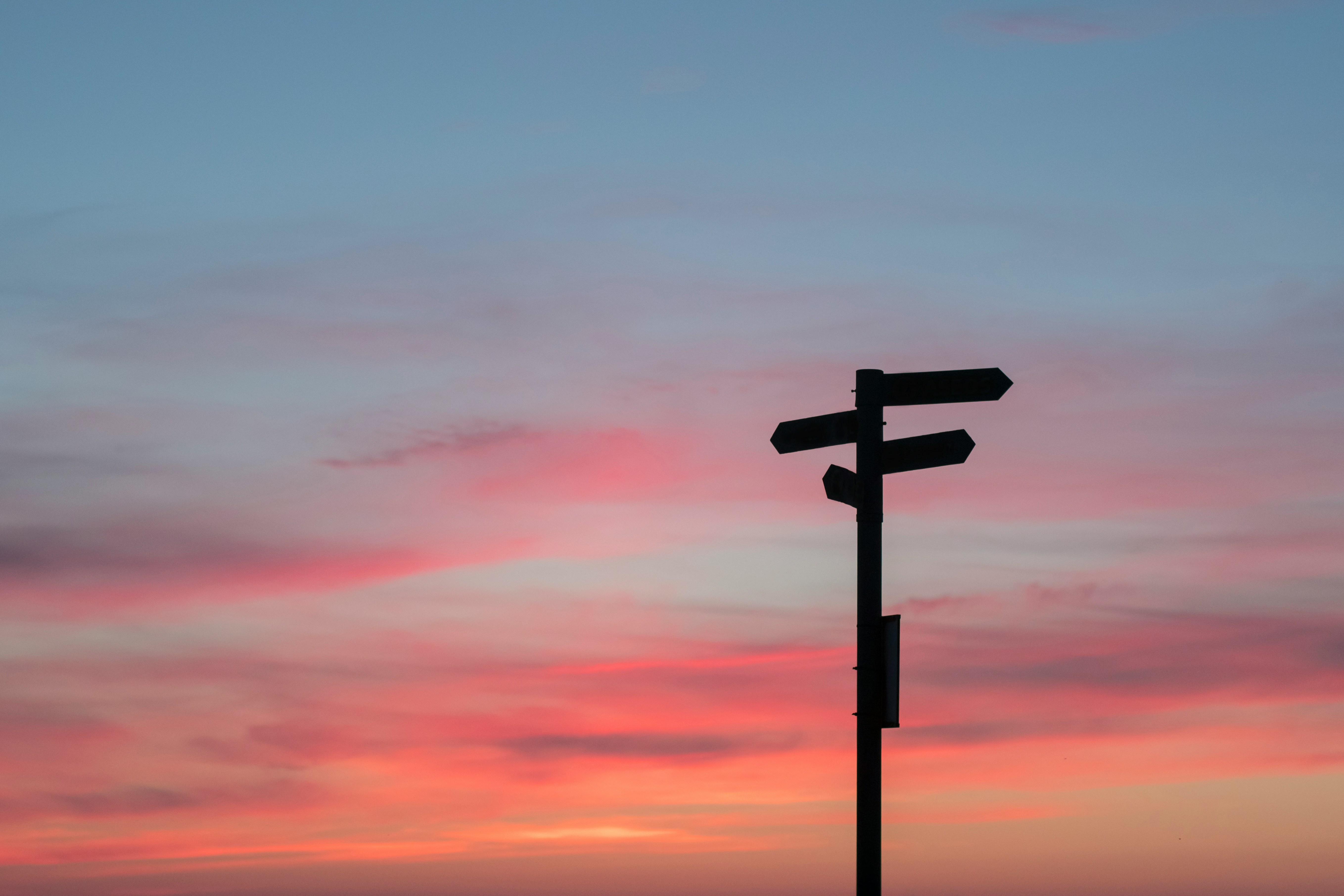 Silhouette of a directional signpost against a pink and orange sunset sky, symbolizing a shift in direction